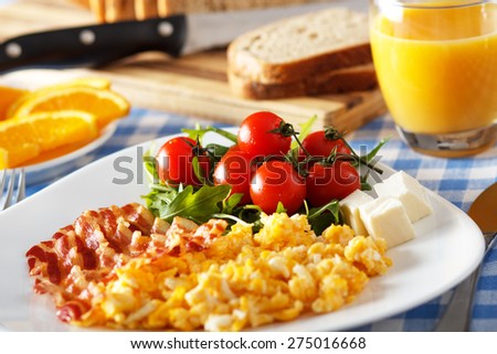 Closeup of a breakfast table with bacon, scrambled eggs, fruit and orange juice.