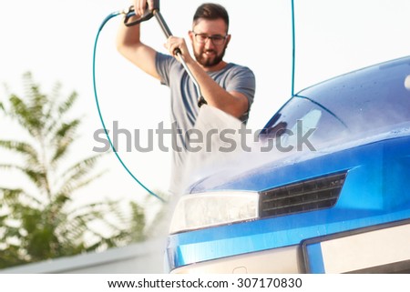 Man washing his car with using a high pressure water jet. Focus on car.