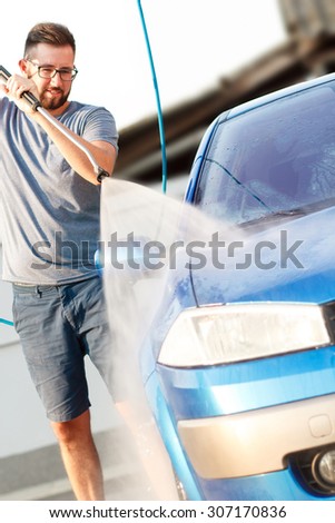 Man washing his car with using a high pressure water jet. Focus on nozzle.