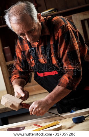 Closeup of a senior carpenter working with a hammer, chisel and wood carving tools.