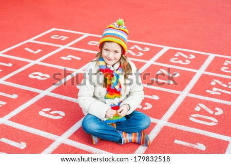 Outdoor portrait of a cute little girl wearing jacket and colorful hat and scarf