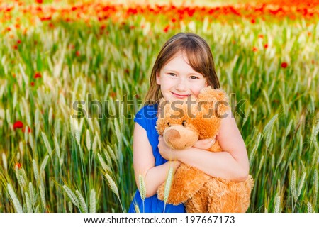 Summer portrait of a cute little girl playing with teddy bear in a wheat field