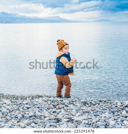 Cute toddler boy playing next to lake on a cold day