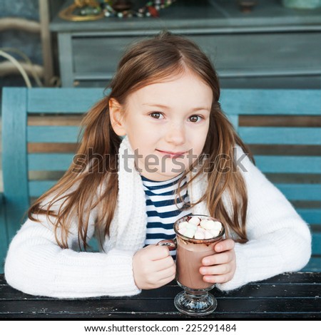 Cute little girl drinking hot chocolate in a cafe on a cold day