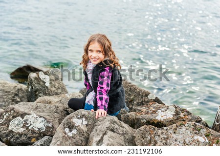 Outdoor portrait of a cute little girl playing next to lake on a fresh day
