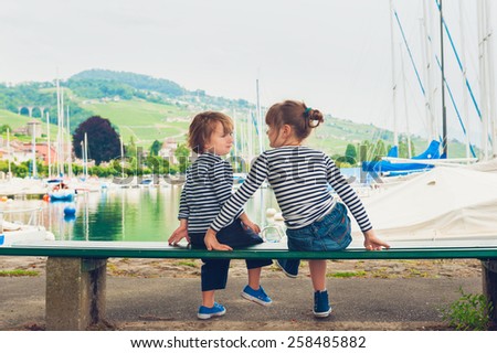 Two kids, little girl and boy resting by the lake, wearing frocks and blue shoes