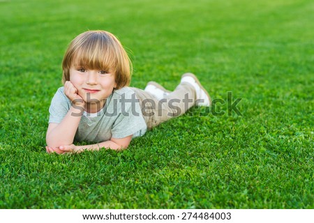 Outdoor portrait of adorable little blond boy laying on a bright fresh green lawn