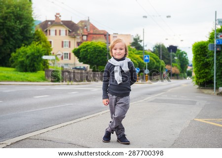 Outdoor portrait of a cute fashion boy in the street, wearing, grey clothes and dark blue shoes