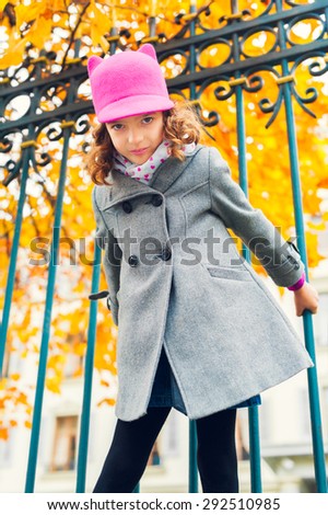 Lovely little girl playing outdoors, wearing grey coat and pink hat with ears