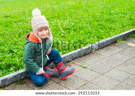 Outdoor portrait of a cute little boy of 3 years old, wearing warm coat, hat and boots