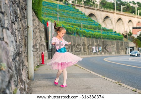 Outdoor portrait of a cute little girl of 7 years old, walking to dance school and dancing in the street, wearing purple ballet dress