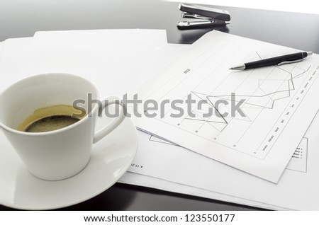Side view of a graph document, coffee and a pen on a black office desk.