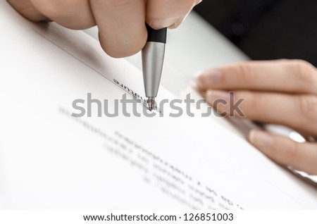 Detail of a female hand signing a contract above signature line.