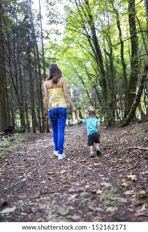 Rear view of young mother and her toddler son spending quality time together walking in the woods.