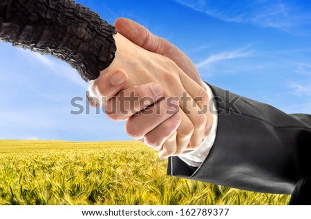 Closeup of male and female hand shaking hands over beautiful wheat field. Concept of successful business of a farmer.