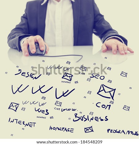 Businessman using a computer mouse sitting at a glass topped desk covered in hand-drawn computing, business and e-commerce icons and notations in a conceptual image. With retro filter effect.