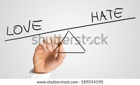 Man drawing a seesaw showing an imbalance between Love and Hate with the word positive being weighted more than the word negative on opposites ends. Concept of love conquering hate.