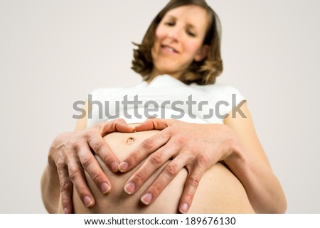 Pregnant woman making a heart gesture with her hands as she tenderly cradles her swollen belly and bonds with her unborn baby, low angle view.