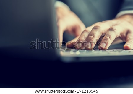 Low angle view from the back of the computer of a businessman typing on a laptop computer keyboard in a retro vintage toned image.