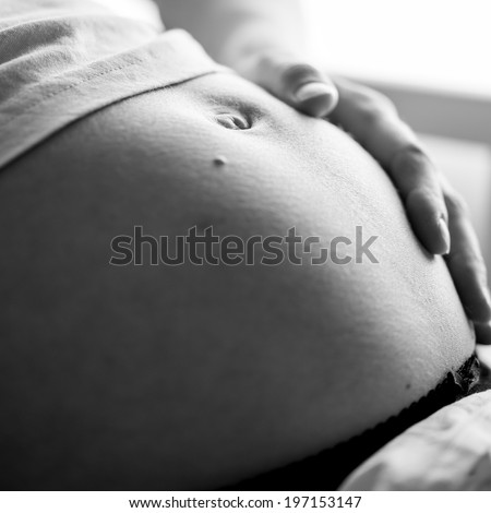Greyscale image of pregnant woman touching her swollen belly and bonding with her unborn child.