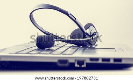 Retro image of black headset on laptop keyboard. Conceptual of customer support or online chat, discussion or conference.