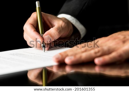 Closeup of male hand signing legal or insurance document on black desk with reflection.