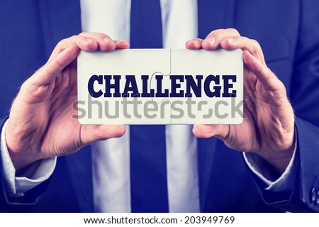 Man holding up two interlocked puzzle pieces with the word - Challenge - on them as he shows that there is a solution and answer and a way to success, toned retro or instagram effect.