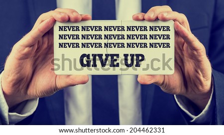 Close-up of the hands of a man wearing business formal suit, with white shirt and tie, while holding two joined jigsaw puzzle pieces with the inspirational message and urge to never give up.