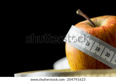 Close-up of a fresh tasty apple, natural source of vitamins and minerals, wrapped with a white measuring tape, with copy space on black, concept of dieting and healthy nutritious food.