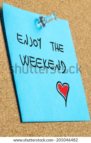 Perspective close-up of a blue reminder with handwritten wish to enjoy the weekend and a red heart shape, pinned on a wooden board, concept of spare time, love and recreation.