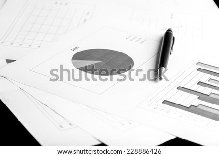 Stylish ballpoint pen lying on a desk on a set of pie and bar graphs in a concept of business analysis, planning and strategy.