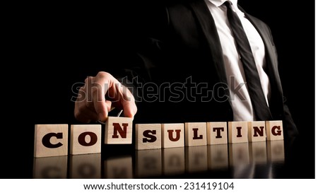 Consultant in Black Business Suit Arranging Small Wooden Pieces with ConsultingText on Black Background.
