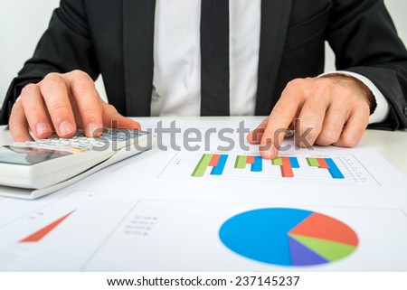 Front view of the hands of a accountant analysing a bar graph using a manual calculator to check the statistics and projections.