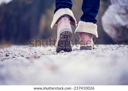 Low angle view of the feet of a woman in jeans and ankle high leather boots walking along a rural path away from the camera, vintage effect toned image.