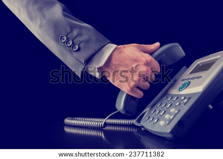 Retro image of businessman making a phone call holding the handset receiver of a telephone in his hand , close up view of his hand in a suit.