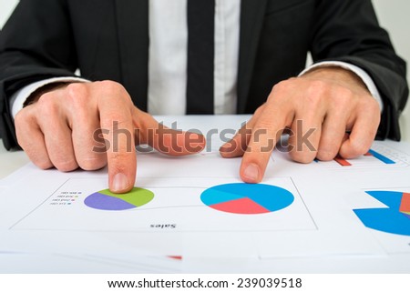 Hands of a businessman analysing two pie graphs as he sits at his desk pointing to one pie graph, in a business strategy concept.