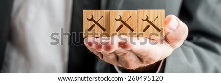 Close up Conceptual Businessman Showing Wooden Blocks on his Hand with Service Tools Prints.