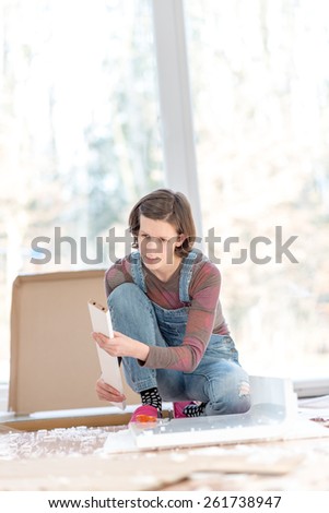 Competent young woman doing DIY renovations kneeling working on the floor in her living room in front of large bright windows with copyspace.