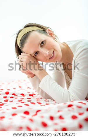 Attractive young woman wearing an headband in her hair leaning on her elbows on a colourful duvet with red polka dots smiling at the camera.