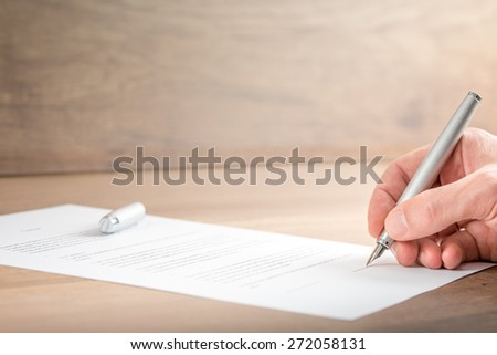 Close up Hand of a Businessman Signing a Contract Document on Top of a Wooden Table.