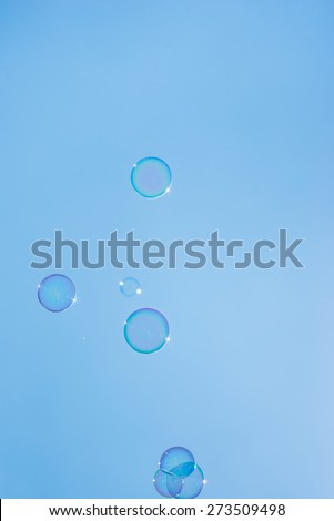 Pretty transparent iridescent bubbles floating against a sunny clear blue sky in a conceptual image.