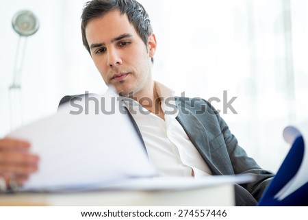Successful young executive in a jacket sitting reading a report or document or employment application with a serious expression as he analyses the information.