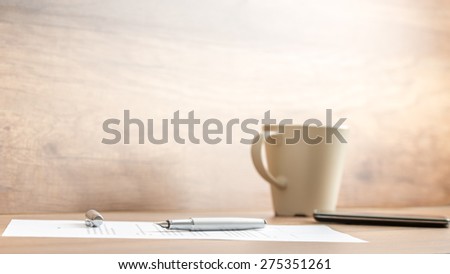 Fountain pen lying on office paperwork alongside a mug of coffee viewed low angle against a rustic or vintage style wall with copyspace.