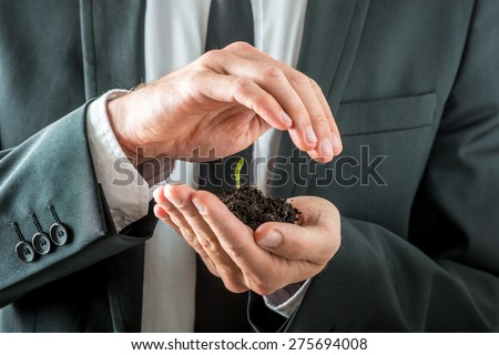 Businessman nurturing a germinating seedling in rich fertile soil cupping it in his hand while covering it with the other conceptual of awareness of conservation of the planet.