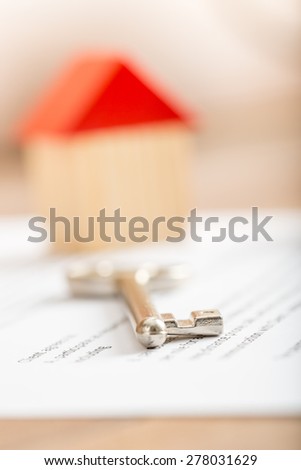 Silver house key lying on a contract for purchase, lease, insurance or mortgage in a real estate concept, viewed low angle with focus to the tip.
