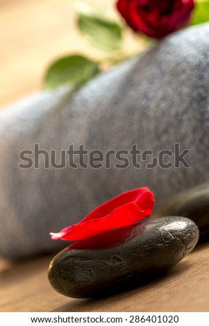 Close up Red Rose Petal on Top of Glossy Spa Stone beside a Rolled Towel on the Floor.