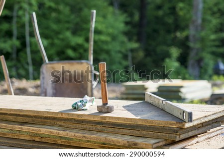 Construction Site concept with a wooden mallet, level and gloves on planks of wood outdoors in a forested area.