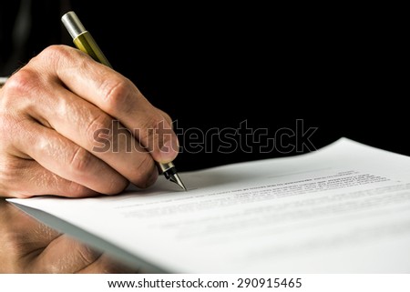 Closeup of male hand signing a contract, employment papers, legal document or testament. Isolated over black background.