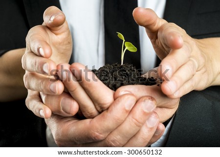 Male and female business partners nurturing a new plant united to protect a green fragile sprout grown in fertile soil, concept of ecology and business start up.