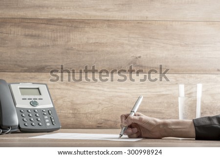 Closeup of female lawyer or executive signing a contract, placed on desk, near the telephone, with copy space on wooden wall.